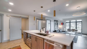 Une cuisine moderne dotée d’un îlot central, d’appareils électroménagers en acier inoxydable et de luminaires suspendus.