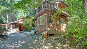 A cabin with a porch and a small deck, surrounded by trees and a gravel path. - Leavenworth Cabin w/ Private Hot Tub! (Leavenworth)