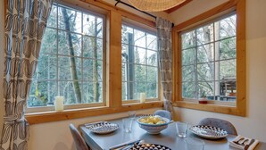 A dining table with patterned plates, bowls, and cutlery, set against a window with a view of trees. - Leavenworth Cabin w/ Private Hot Tub! (Leavenworth)
