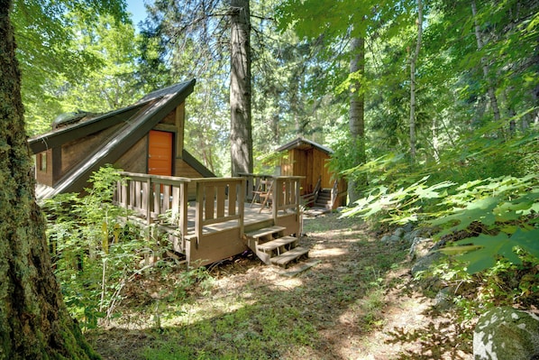 A forest cabin with a wooden deck and a staircase leading to the entrance.