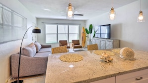 A modern kitchen with a granite countertop, a dining table with placemats, a sofa, and a ceiling fan.