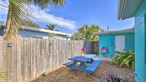 A backyard with a wooden fence, a picnic table with a lantern, and a turquoise building with a door.