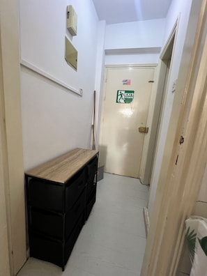 A narrow hallway with a wooden bench, a black storage unit, and a door with an exit sign.