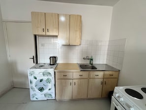 Une cuisine de taille réduite, dotée de meubles en bois, d’un évier en acier inoxydable et d’un dosseret de carrelage blanc.