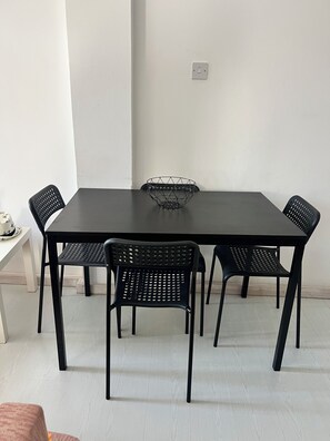 Ein Essbereich mit einem schwarzen Tisch, vier schwarzen Stühlen und einem Drahtkorb auf dem Tisch.