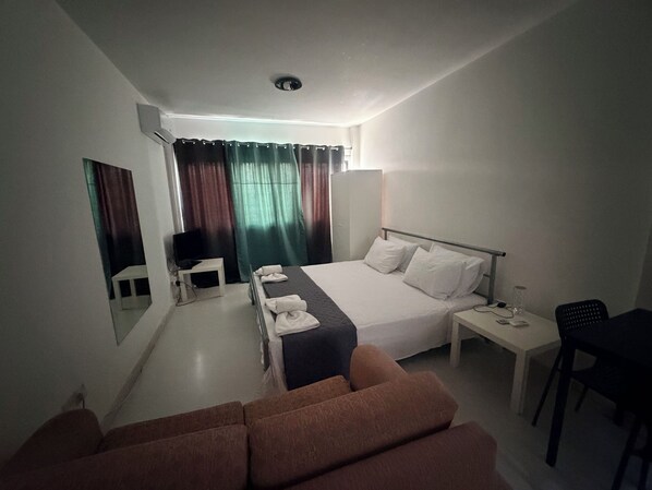 A hotel room with a bed, a desk, a chair, a TV, and a sofa.