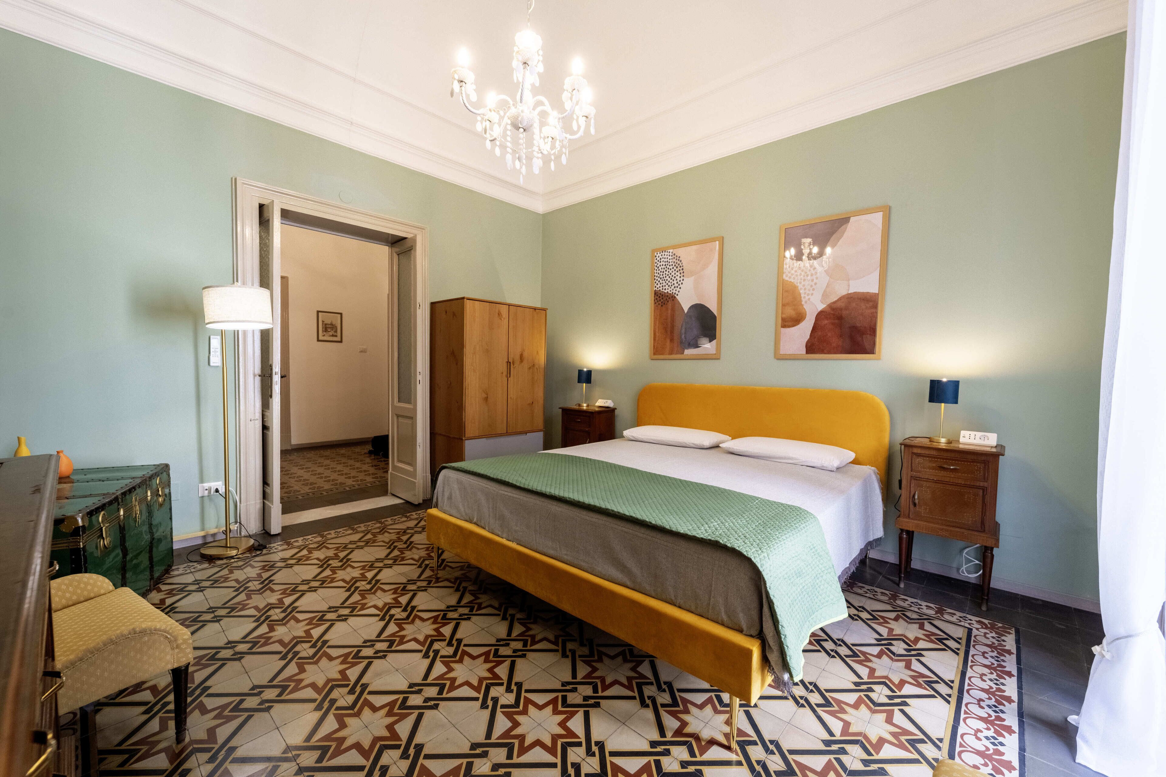 A bedroom with a bed, a dresser, a lamp, and a door leading to another room.