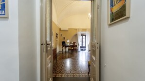 A hallway with a patterned floor leading to a room with a desk and chairs.