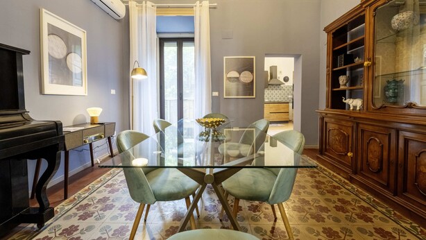 A dining area with a glass table and chairs, a piano, and a cabinet with decorative items.