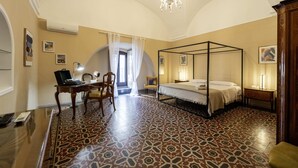 A four-poster bed with a canopy, a desk with a laptop, and a patterned floor.