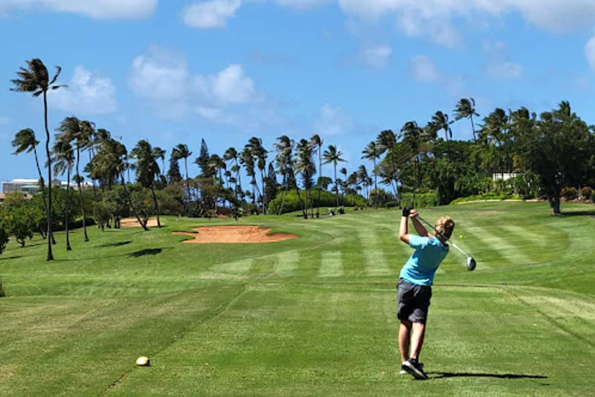 Ein Golfplatz bei blauem Himmel, mit Palmen und einem Golfer, der im Schwung ist.