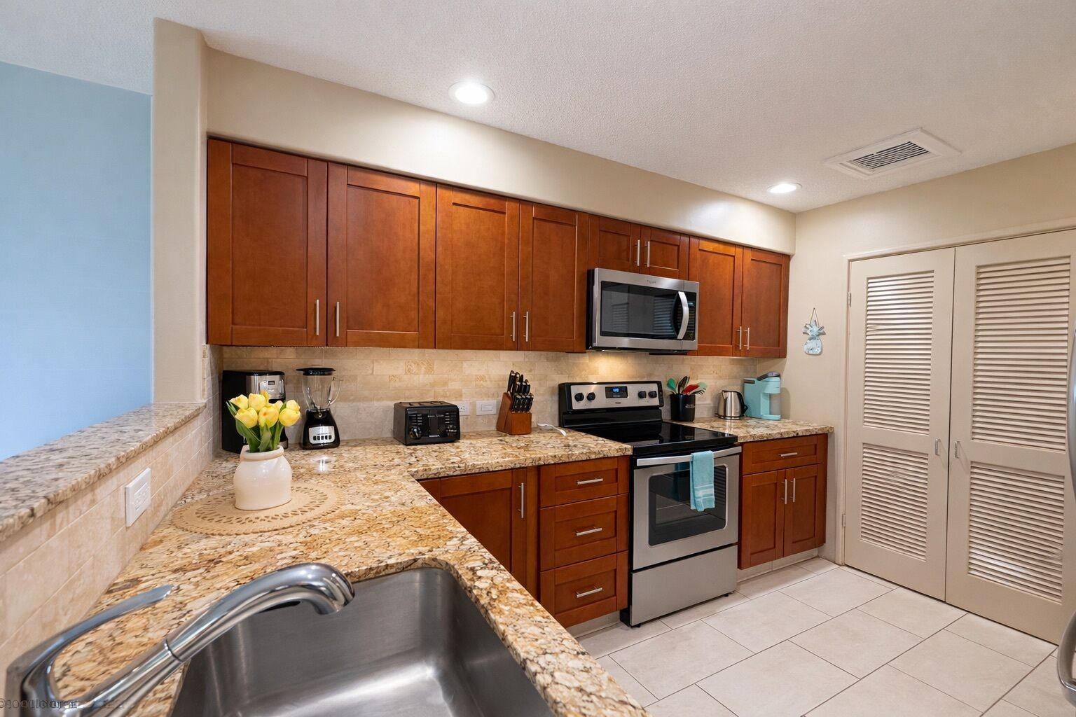 A kitchen with granite countertops, wooden cabinets, a microwave, a toaster, a blender, and a sink.