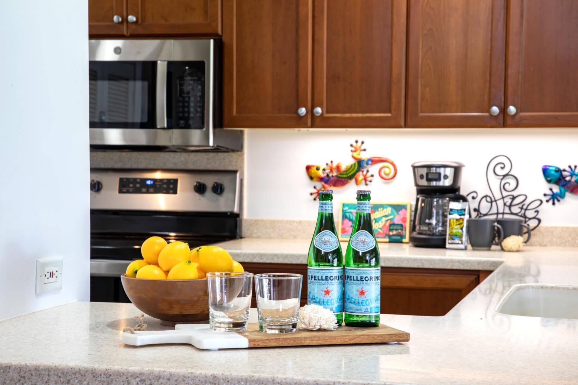 A kitchen counter with lemons, two bottles of Pellegrino water, a glass, and a cutting board.