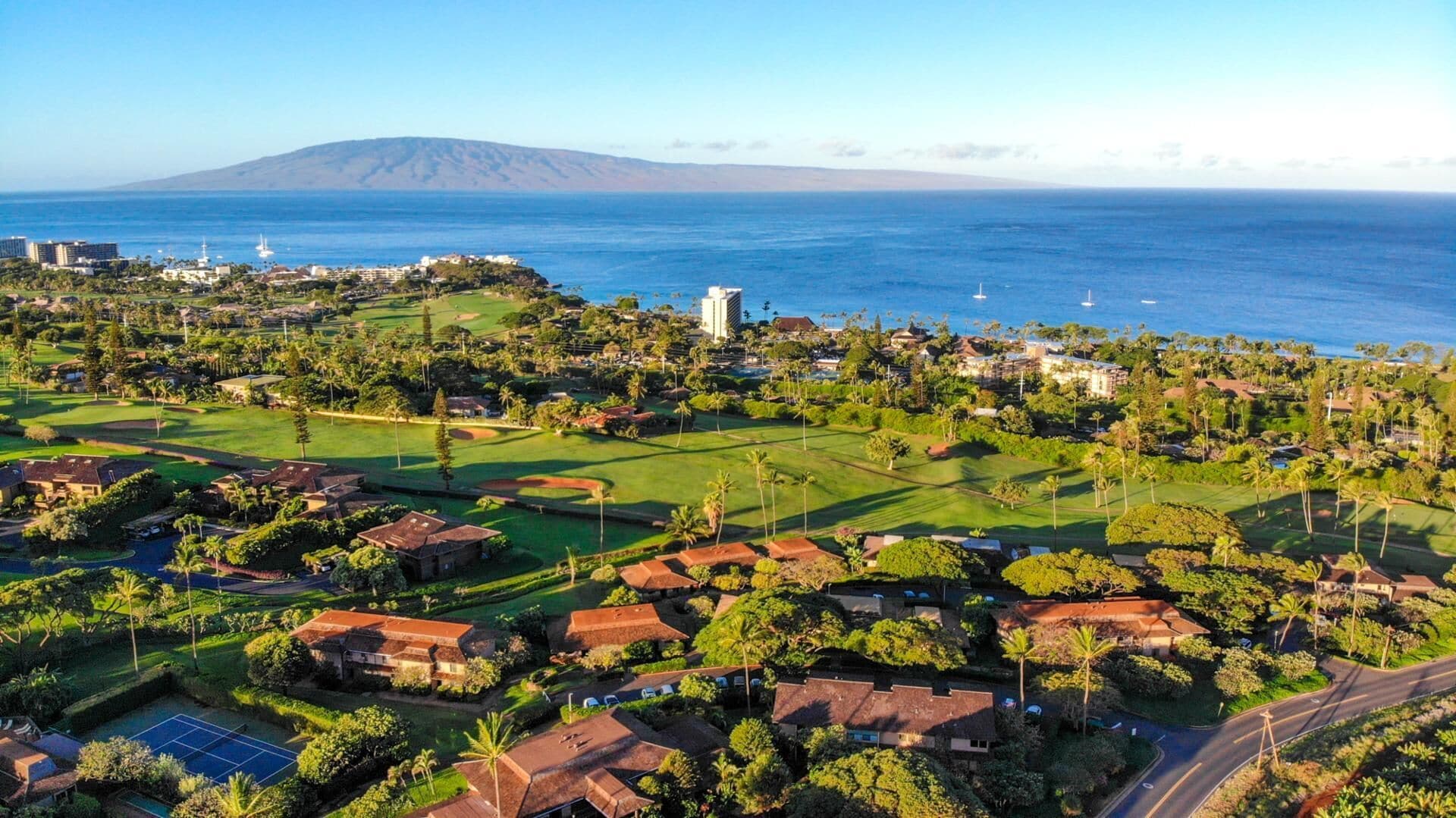 An aerial view of a coastal resort with golf courses, beachfront properties, and a prominent mountain in the background.