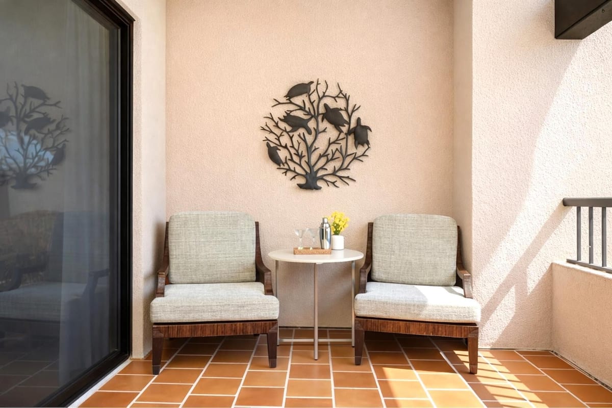 Ein kleiner Patio-Bereich mit zwei Stühlen, einem runden Tisch und einer Wanddekoration mit Baumdesign.