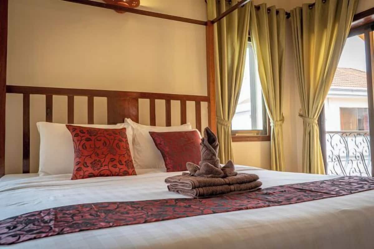Een hotelkamer met een bed, kussens, een dekbed en gordijnen.