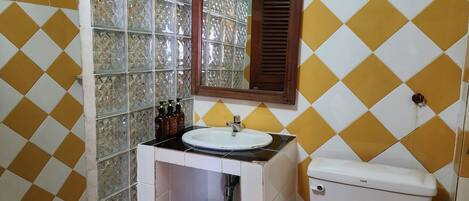 A bathroom with a white sink, mirror, and toilet. The walls are tiled with a yellow and white diamond pattern.