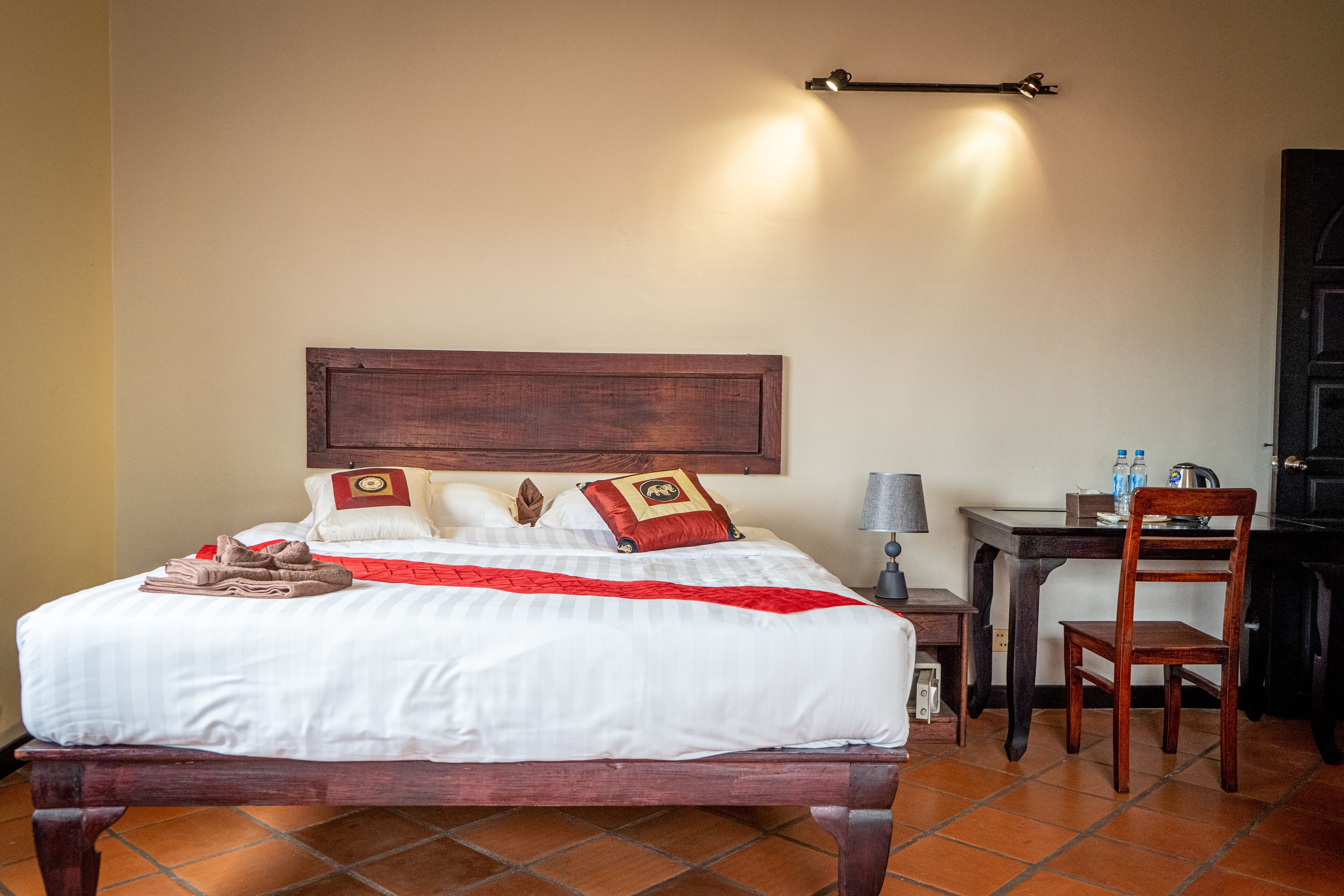 A neatly made bed with a wooden headboard, a small table with a lamp, and a chair.