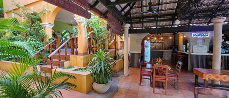 Un restaurante con zona de bar, mesas al aire libre y una escalera rodeada de vegetación.