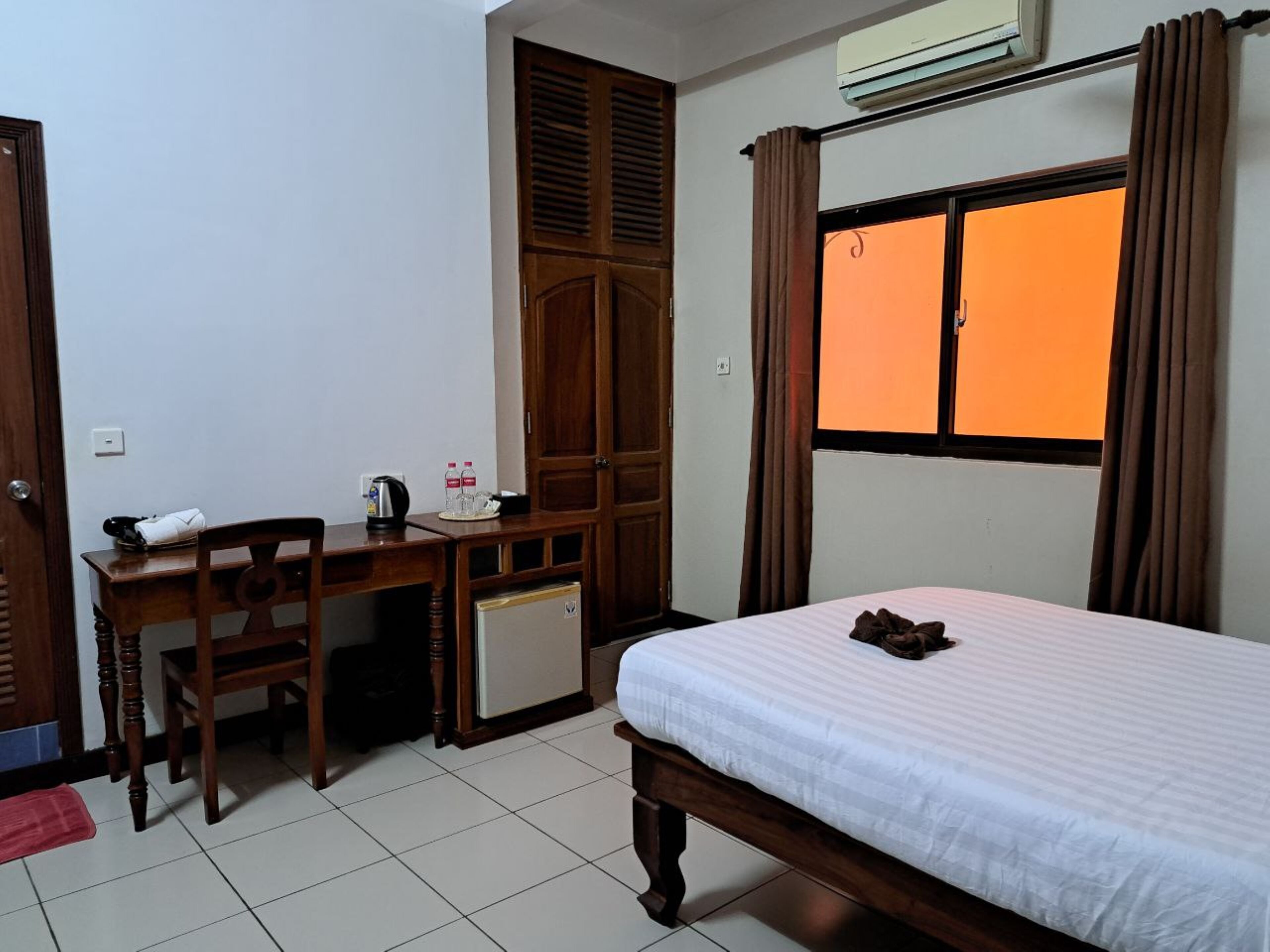 A hotel room with a bed, a desk with a chair, a wardrobe, and a window with curtains.