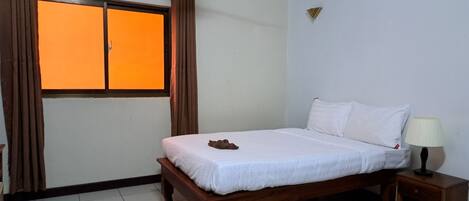 A hotel room with a bed, a nightstand with a lamp, a window with curtains, and a wall-mounted air conditioner.