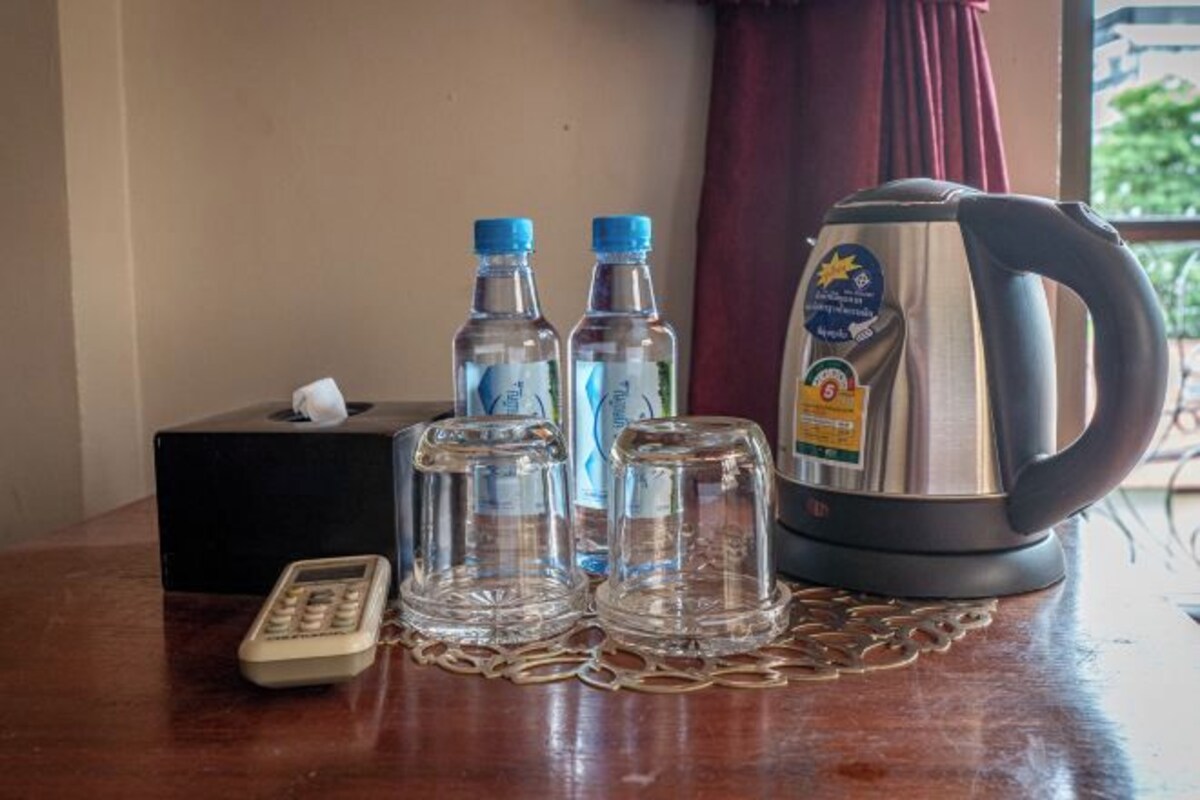 Un tavolo con un portatovassini, due bottiglie d'acqua, un bollitore, un telecomando e una catena decorativa in metallo.
