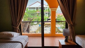 Une chambre avec deux lits, une fenêtre donnant sur une maison et sur la verdure, et une lampe sur une table de chevet.