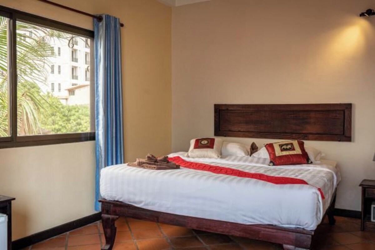 Una camera d'albergo con un letto, una finestra con tende, una testiera e un punto luce fissato al muro.
