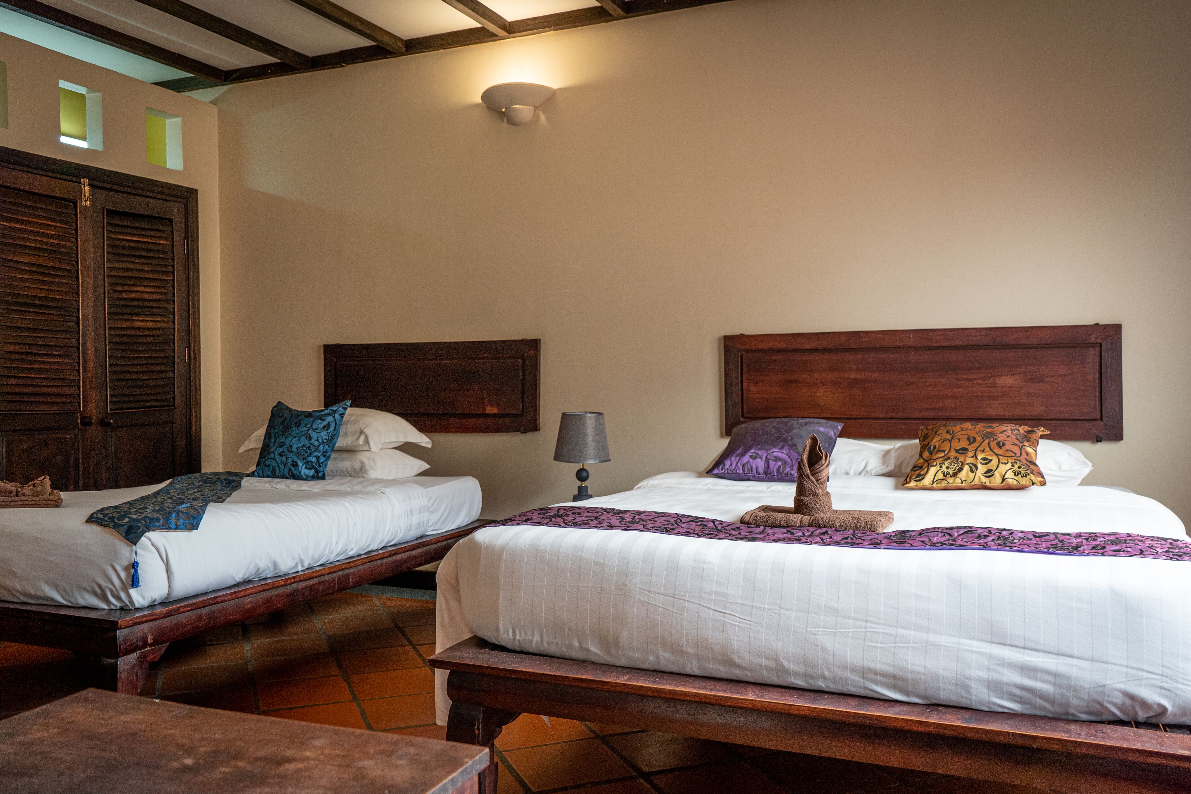 Dos camas contiguas con cabeceros de madera, ropa blanca y almohadones decorativos.