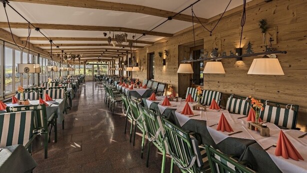 A long dining area with striped tables and chairs, large windows, and wooden beams on the ceiling. - Ferienwohnung, 80m², 2 Schlafzimmer, Balkon Bzw. Terrasse (Eggstätt)