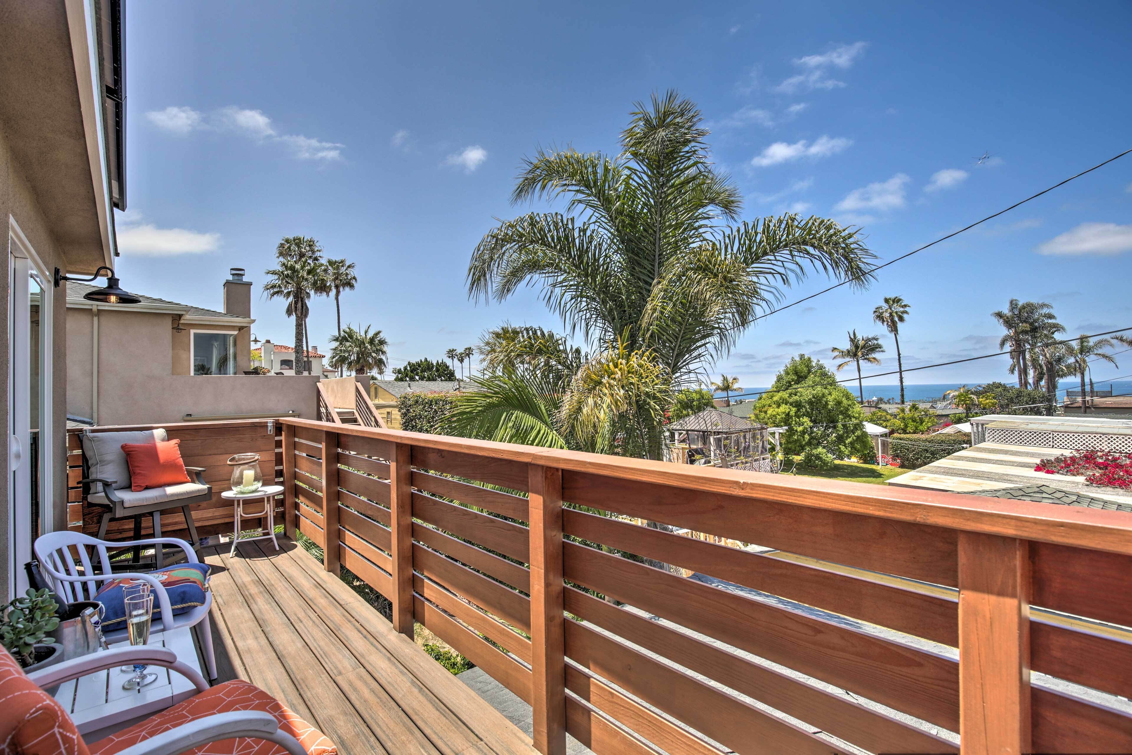 Una terraza de madera con mobiliario exterior, vista a palmeras y cielo despejado.
