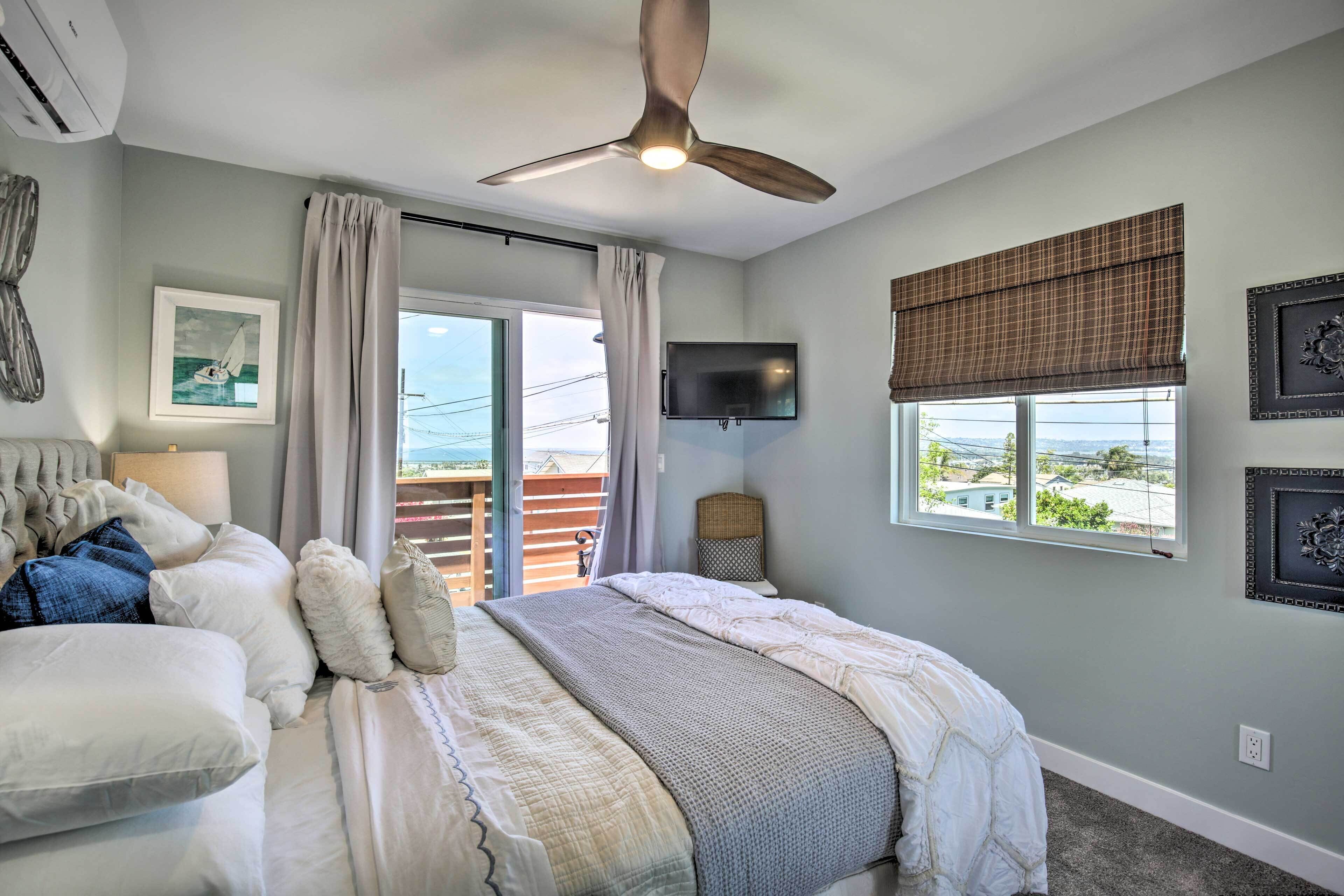 A bedroom with a bed, a ceiling fan, a TV, and a window with a view.