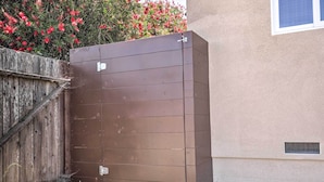 A brown metal gate with a wooden fence and a building with a beige wall and a window. - Dog-friendly San Diego Home - 1 Mi to Ocean Beach (San Diego)