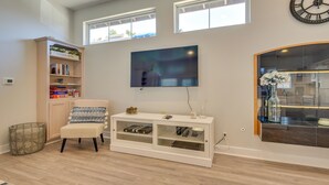 A living room with a white entertainment unit, a bookshelf, a cushioned chair, and a large window with a view. - Luxe Pasadena Casita w/ Fireplace & Grill (Pasadena)