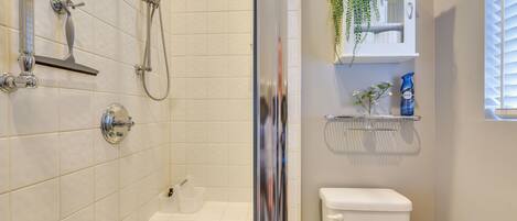 A bathroom with a shower, toilet, and a shelf with toiletries.