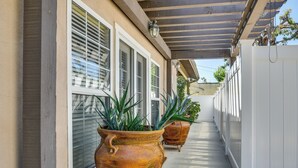 A covered outdoor corridor with large potted plants, white doors, and a concrete floor. - Luxe Pasadena Casita w/ Fireplace & Grill (Pasadena)