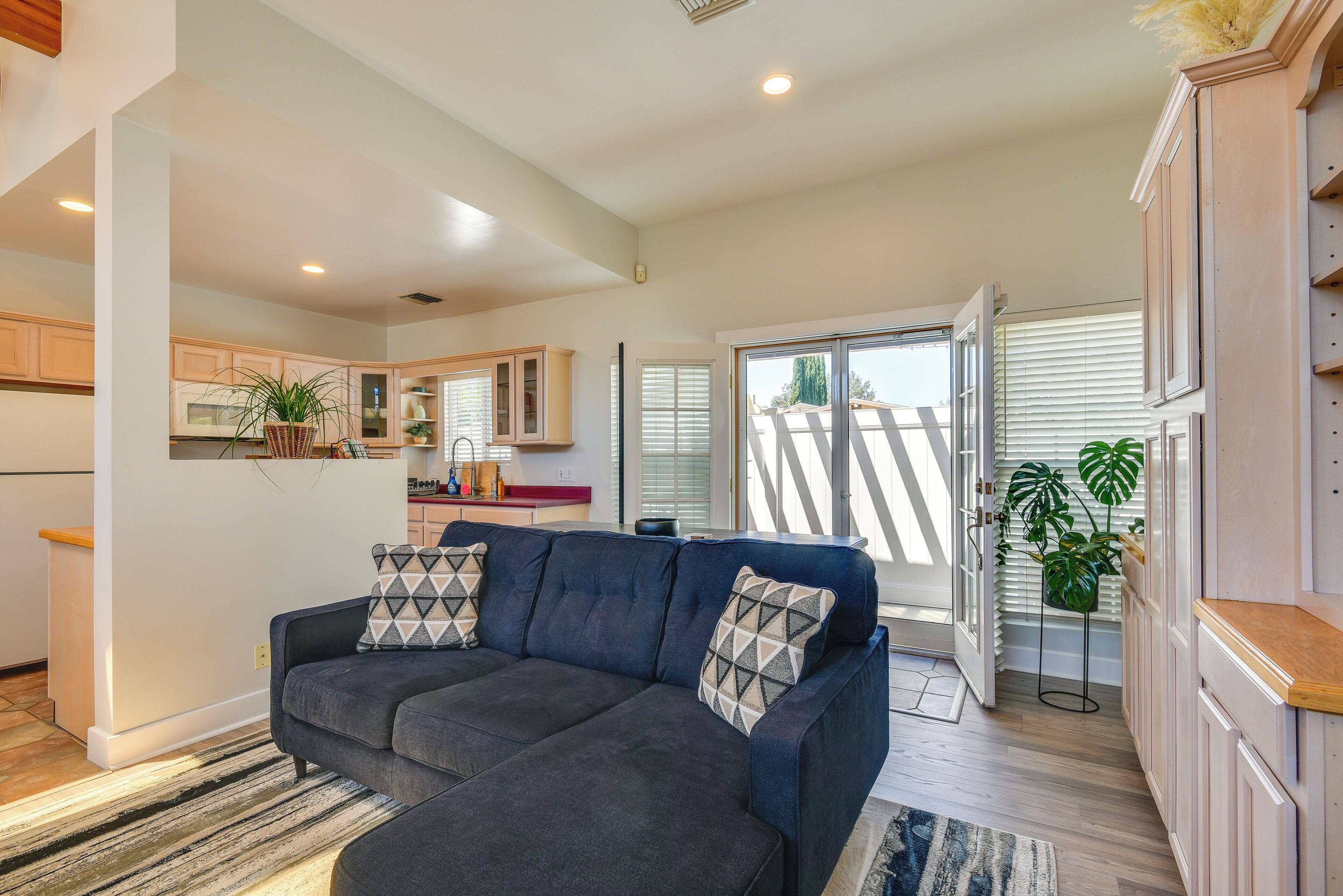 A modern living room with a dark blue sectional sofa, a kitchen in the background, and a sliding glass door leading to a balcony.