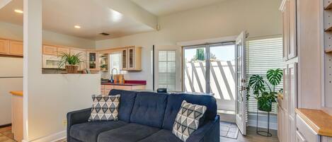 A modern living room with a dark blue sectional sofa, a kitchen in the background, and a sliding glass door leading to a balcony.