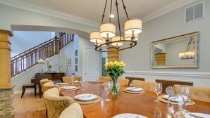 Un comedor con una mesa de madera dispuesta para seis personas, rodeada de sillas tapizadas. Un candelabro cuelga sobre la mesa, y un espejo está montado en la pared a la derecha.