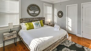 Un dormitorio con cabecera de madera, cama con ropa blanca, almohadas verdes y un adorno en la pared.