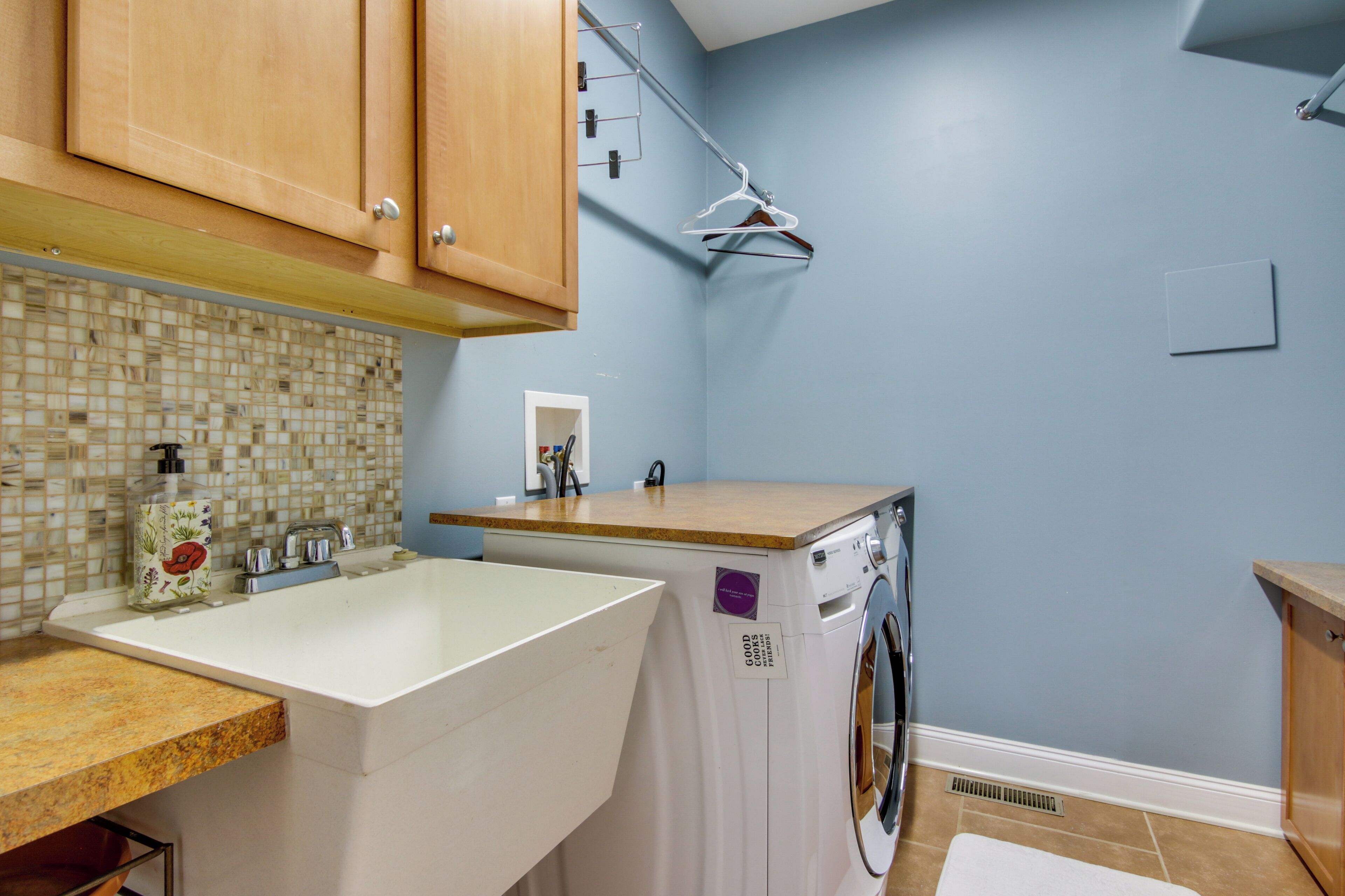 A laundry room with a washing machine, a sink, and wooden cabinets.