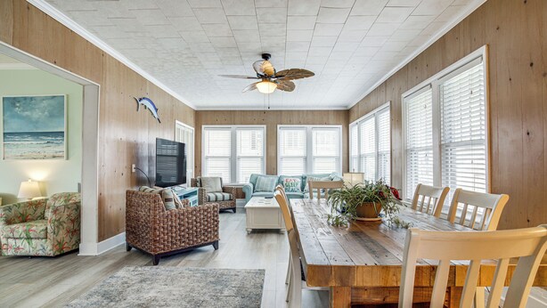 A spacious living room with a wooden ceiling, large windows with blinds, a dining table with chairs, a television, and a beach-themed couch. - Near Beach & Boardwalk! Group Escape in Ocean City (Ocean City)