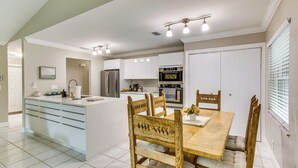 A modern kitchen with white cabinetry, a central island, and a dining area with wooden chairs. - Wellington Vacation Rental: Private Saltwater Pool (Wellington)