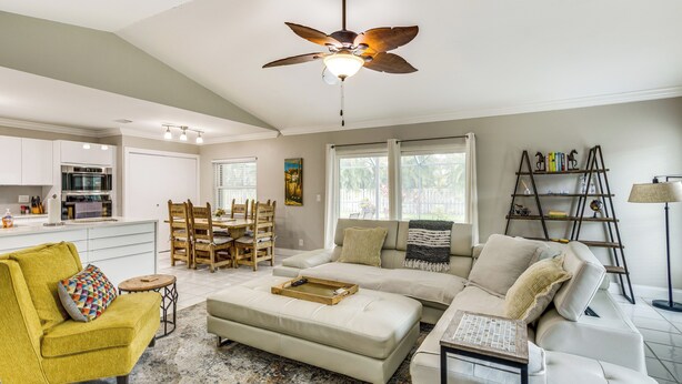 A spacious living room with a sofa, ottoman, and a yellow armchair. There is a dining area with a table and chairs, and a kitchen in the background. - Wellington Vacation Rental: Private Saltwater Pool (Wellington)