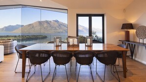 Un comedor con una mesa grande, cuatro sillas y vistas a montañas y un lago.