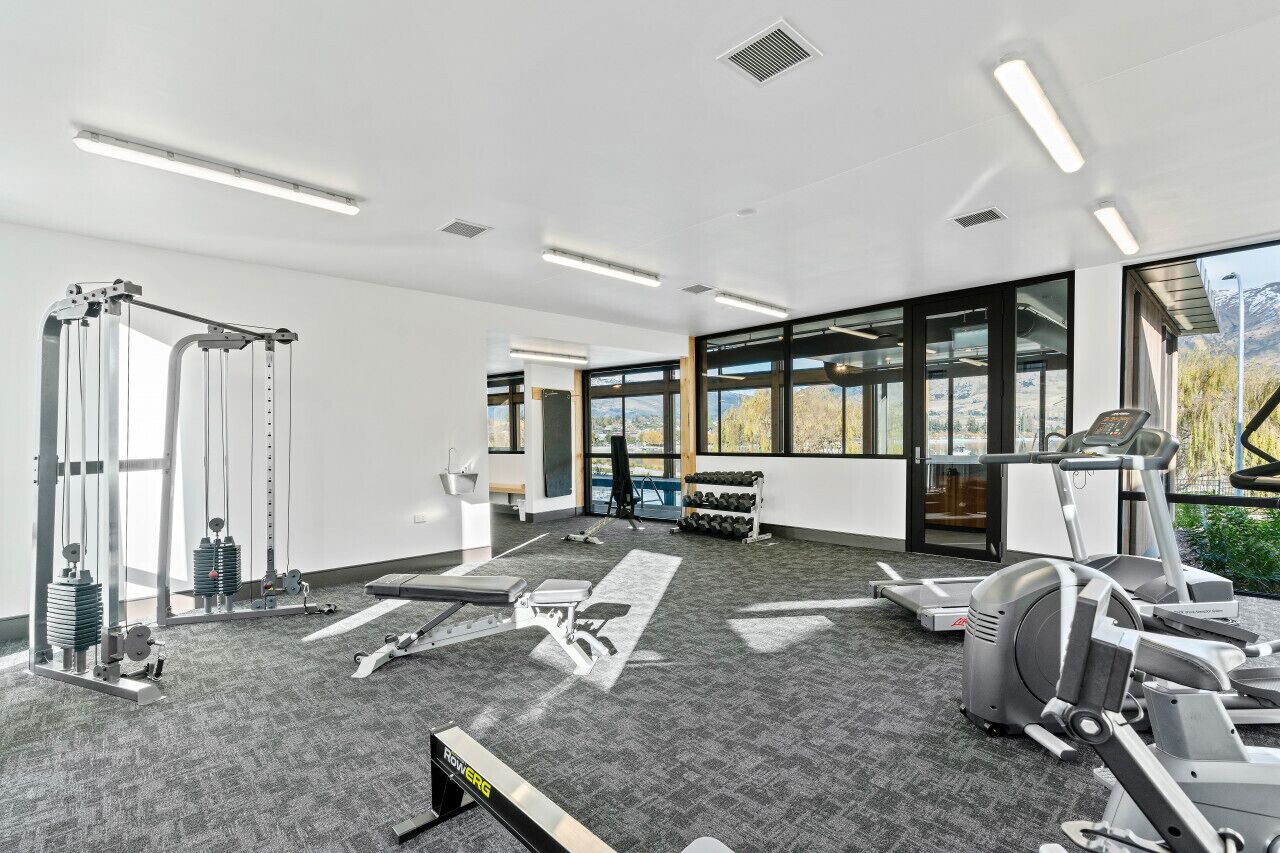 A modern gym with cardio equipment, weight machines, and a large window offering a mountain view.