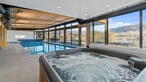 Een modern binnenzwembad met een jacuzzi, grote ramen en uitzicht op bergen.