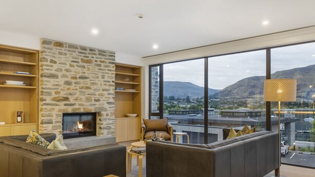 Een moderne woonkamer met een stenen openhaard, grote ramen en uitzicht op bergen.
