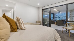 Een moderne slaapkamer met een groot bed en een schuifglazen deur naar een balkon met buitenmeubilair.