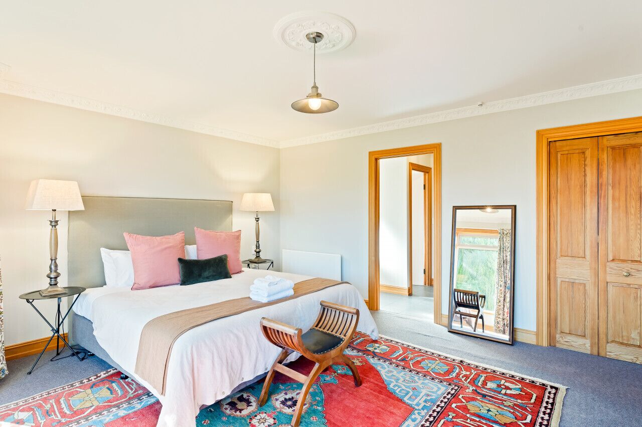 Hotelkamer met een groot bed, twee bedlampen, een houten stoel, een spiegel en uitzicht op het omliggende landschap.